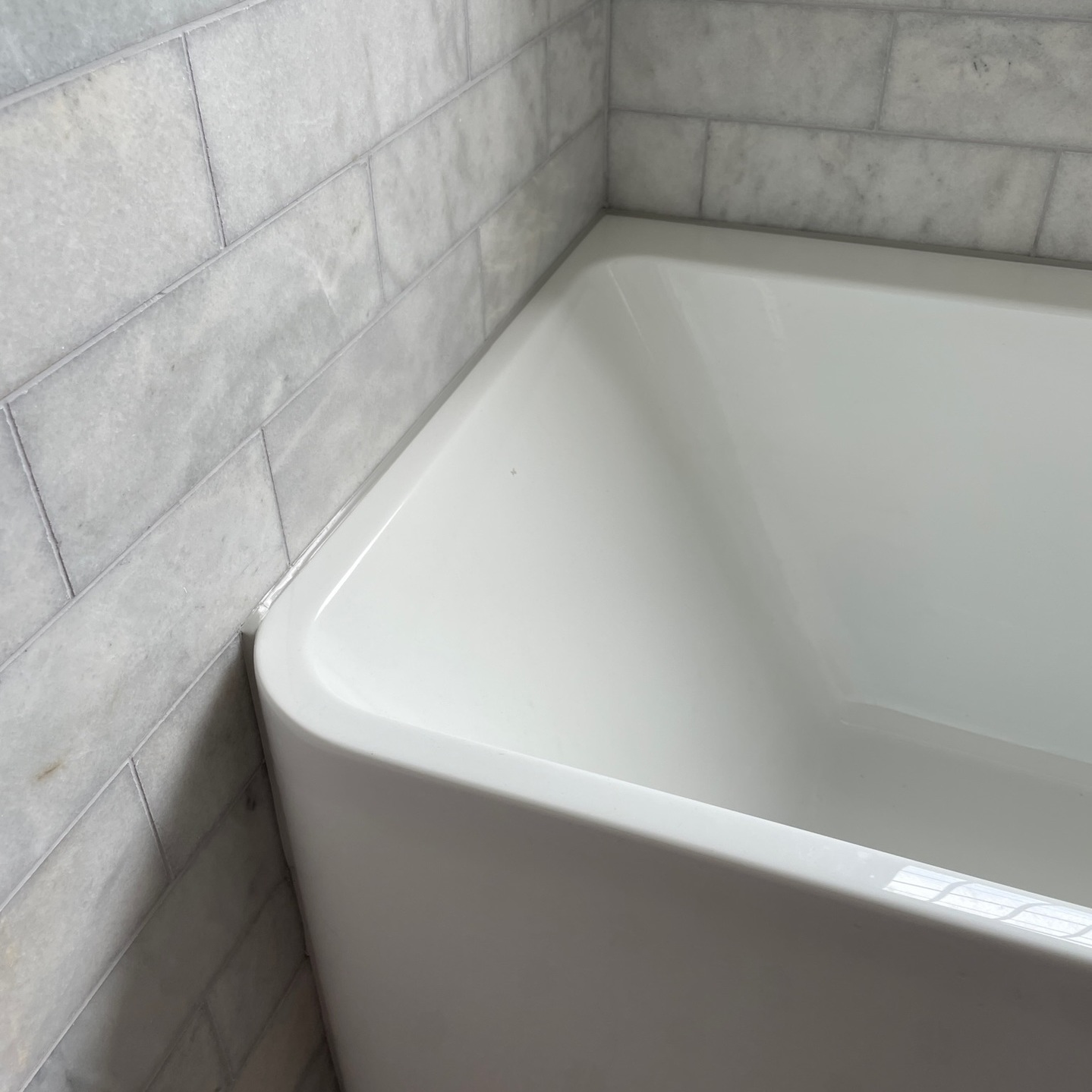 grey mastic on white bath against grey tiles